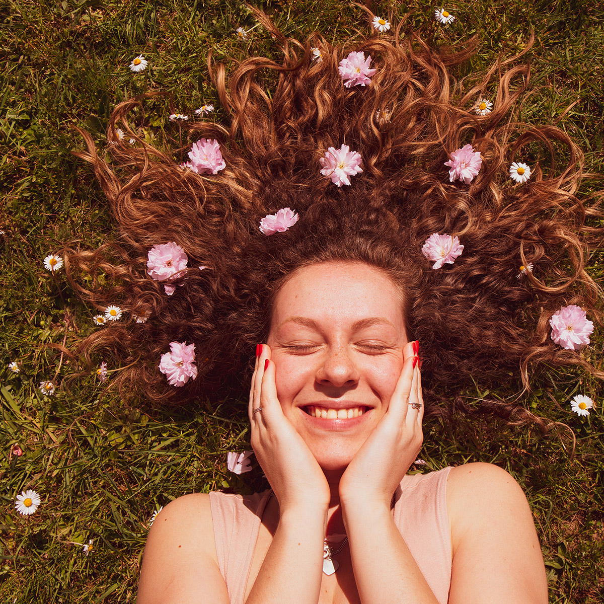Photo d'Aline les cheveux étendu dans l'herbe entroué de fleurs.